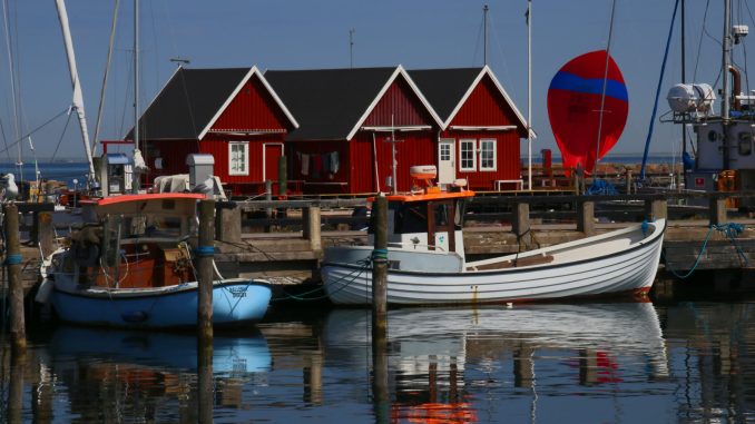 Røde havnehuse og træbåde spejlet i vandet i Dragørs gamle havn