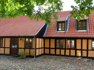 Gult bindingsværkshus med rødt tegltag ved en brostensbelagt gade i Ebeltoft