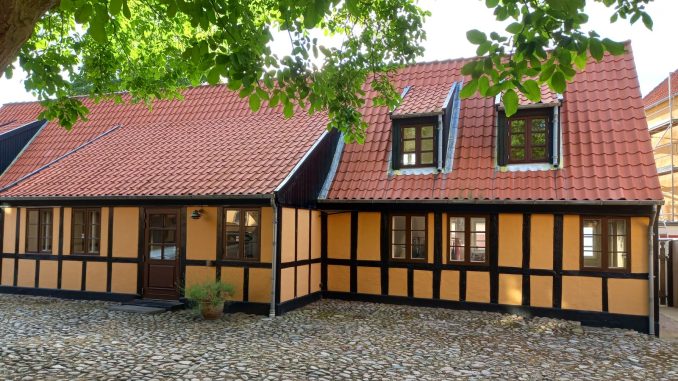Gult bindingsværkshus med rødt tegltag ved en brostensbelagt gade i Ebeltoft